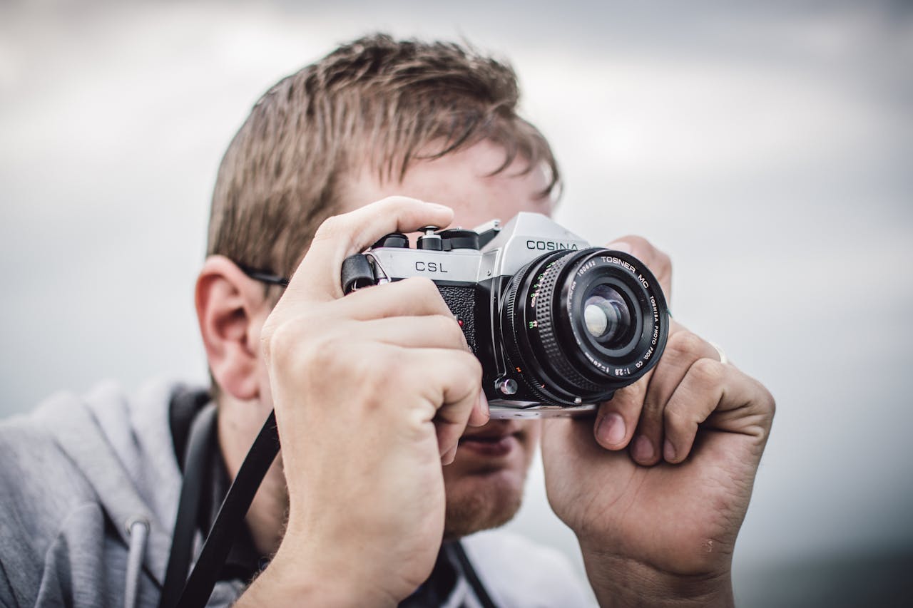 Photographer with vintage Cosina camera taking a picture outdoors.