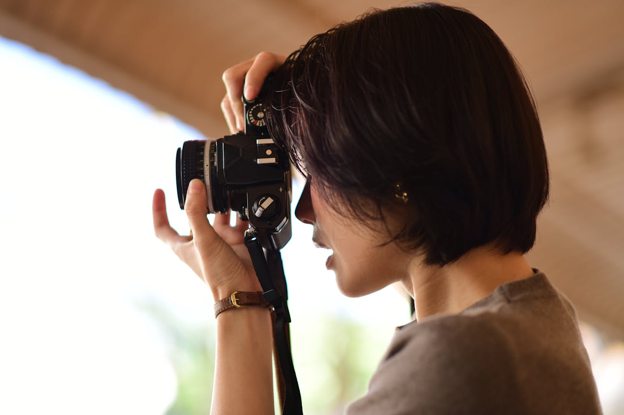 A woman skillfully using a camera to take photos outdoors, demonstrating focus and passion for photography.